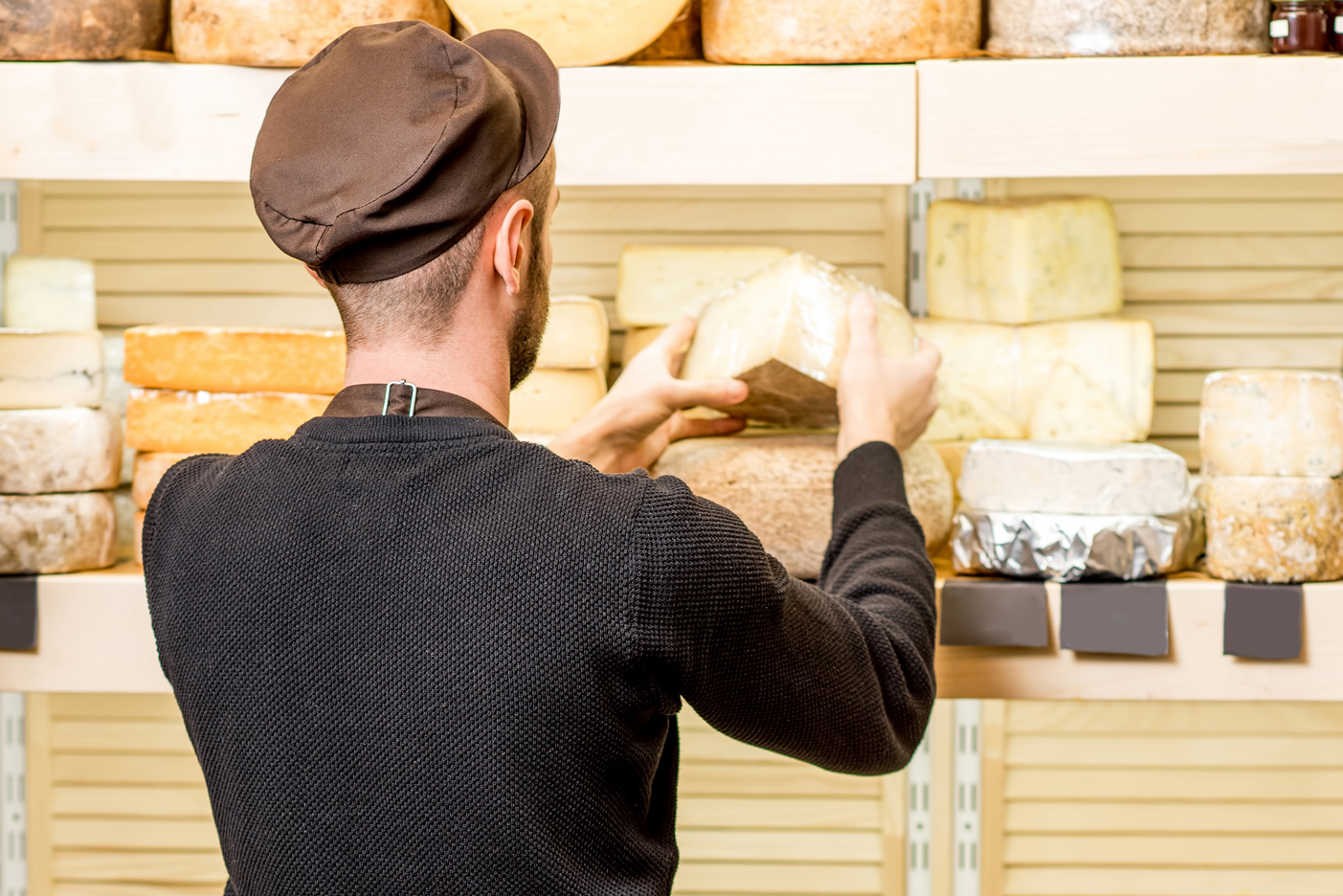 Imagen de un comerciante de quesos de espaldas colocando piezas de queso en estanterías